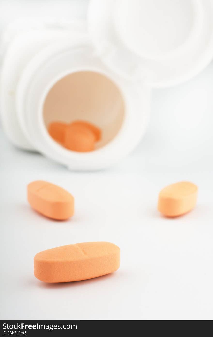 Heap of orange tablets with a jar on white