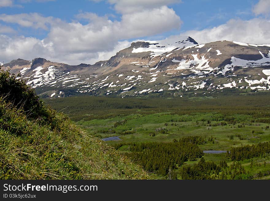 This image shows snowy mountains and a lush valley with several ponds and wetlands in the Glacier National Park area of MT. This image shows snowy mountains and a lush valley with several ponds and wetlands in the Glacier National Park area of MT.