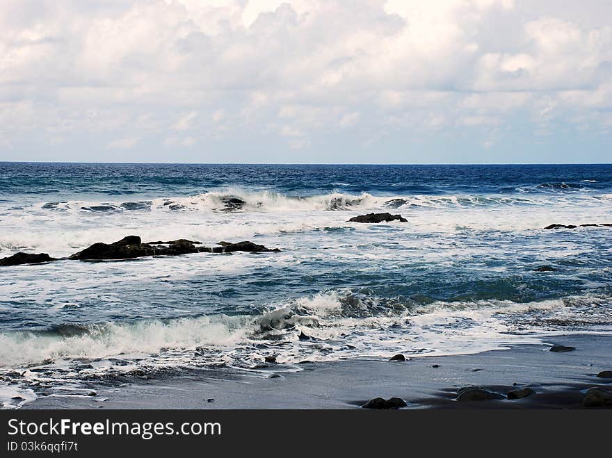 Ocean with waves and stones, sand and blue cloudy sky. Ocean with waves and stones, sand and blue cloudy sky