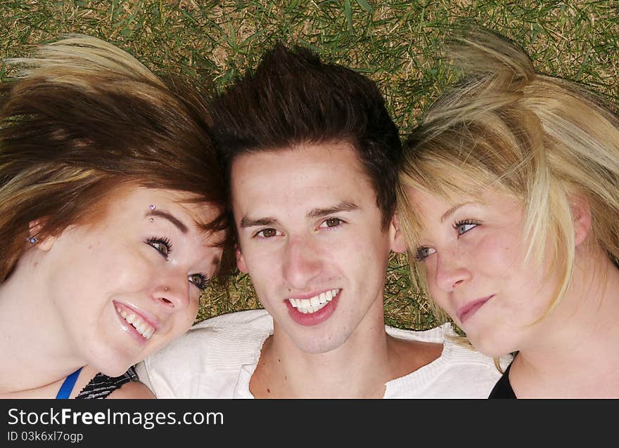 Lucky guy with two adoring girlfriends, close up, head shots. Guy smiling at camera, girls smiling at him. Happy teens laying on grass. Lucky guy with two adoring girlfriends, close up, head shots. Guy smiling at camera, girls smiling at him. Happy teens laying on grass