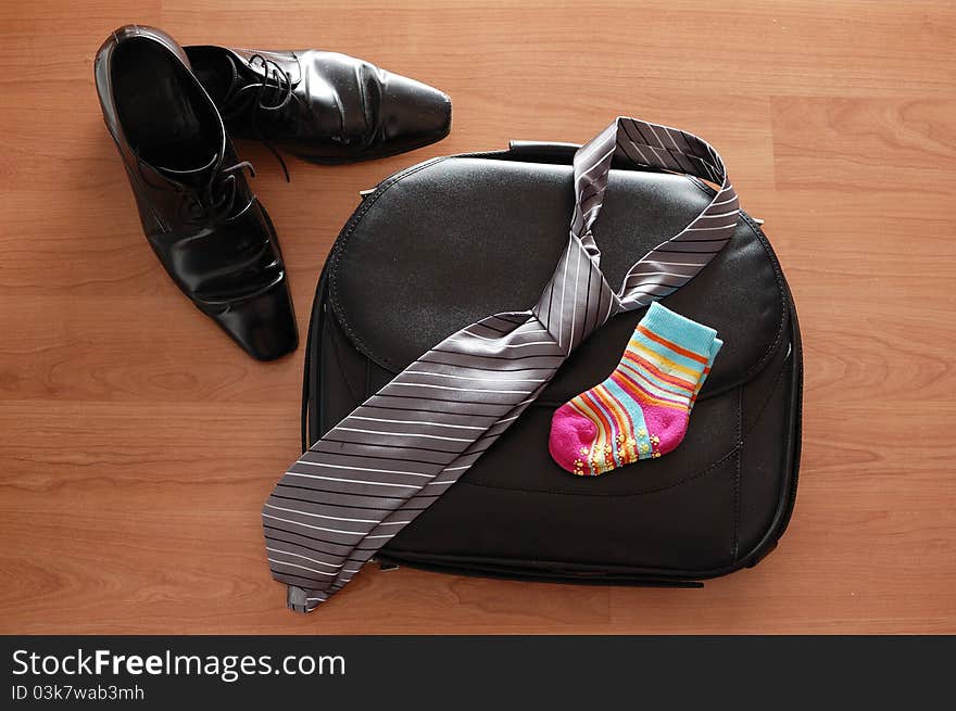 Composition of black shoes, briefcase, tie and kid`s socks on a wooden table. Composition of black shoes, briefcase, tie and kid`s socks on a wooden table