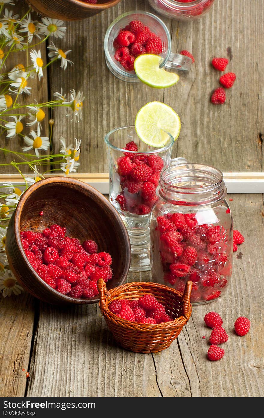 Composition with fresh ripe raspberries in glass, pot, bowl and basket on old wooden table, near mirror with reflex