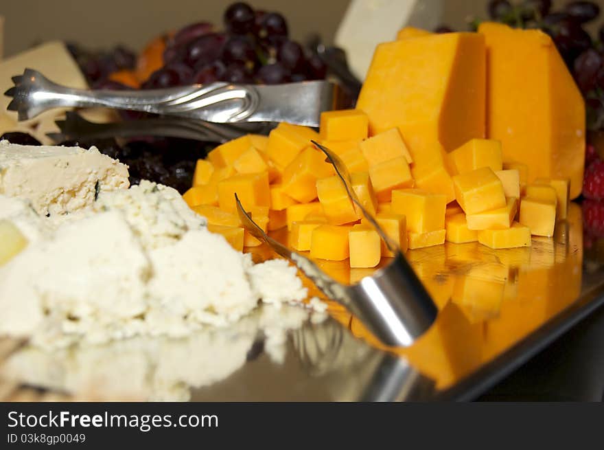 Close up of buffet table focusing on cubed orange cheddar cheese with tongs. Close up of buffet table focusing on cubed orange cheddar cheese with tongs.