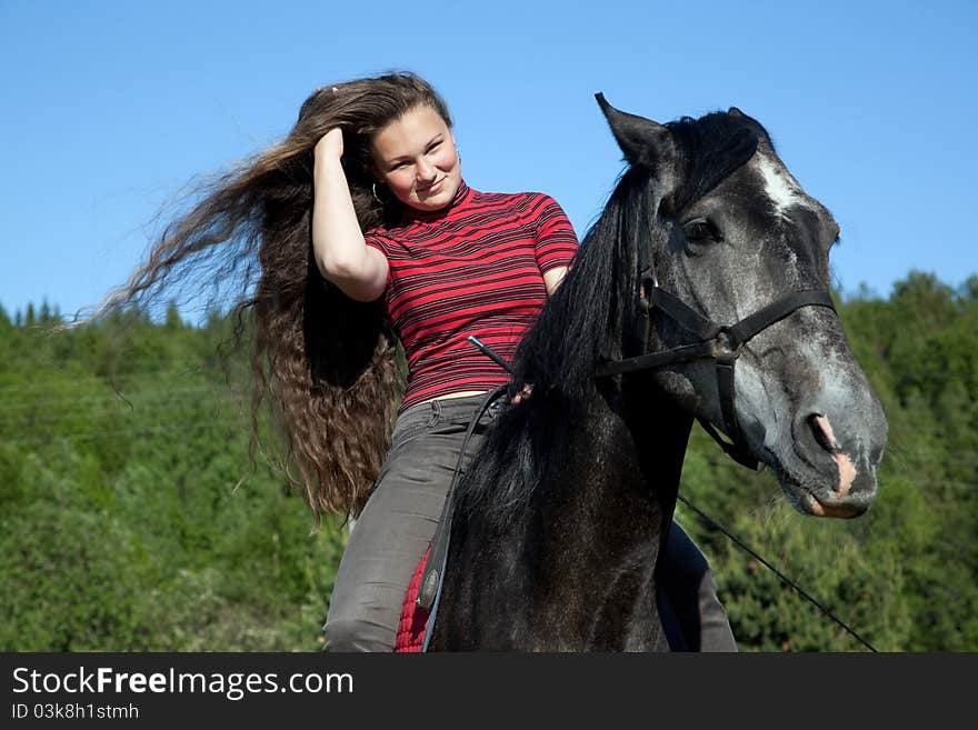 A girl with flowing hair on a black horse in a forest