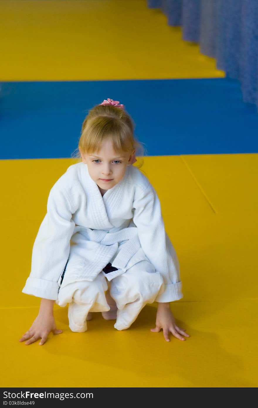 The little girl in a white kimono sits on the mat. The little girl in a white kimono sits on the mat