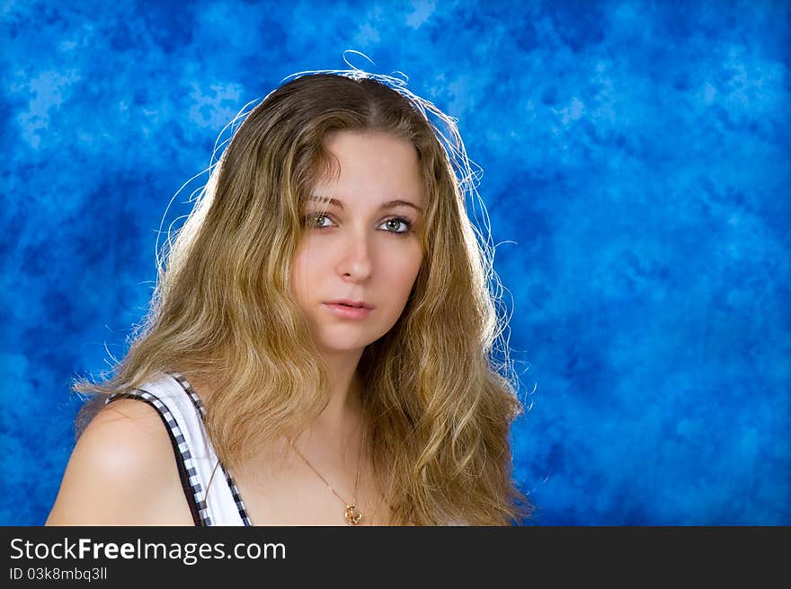 Young pretty girl with long blond hair on a blue background quietly watching us. Young pretty girl with long blond hair on a blue background quietly watching us