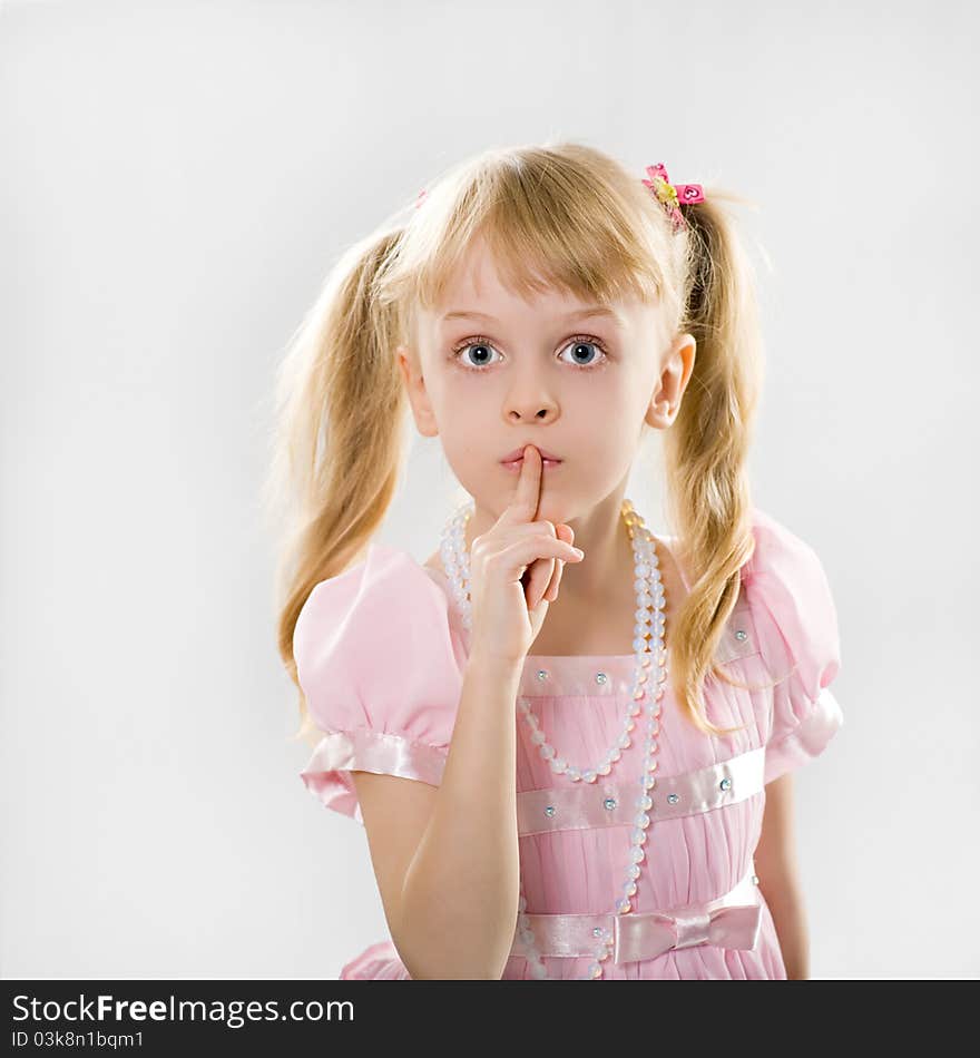 A little girl with long blond hair in a smart pink dress put her finger to her lips. A little girl with long blond hair in a smart pink dress put her finger to her lips