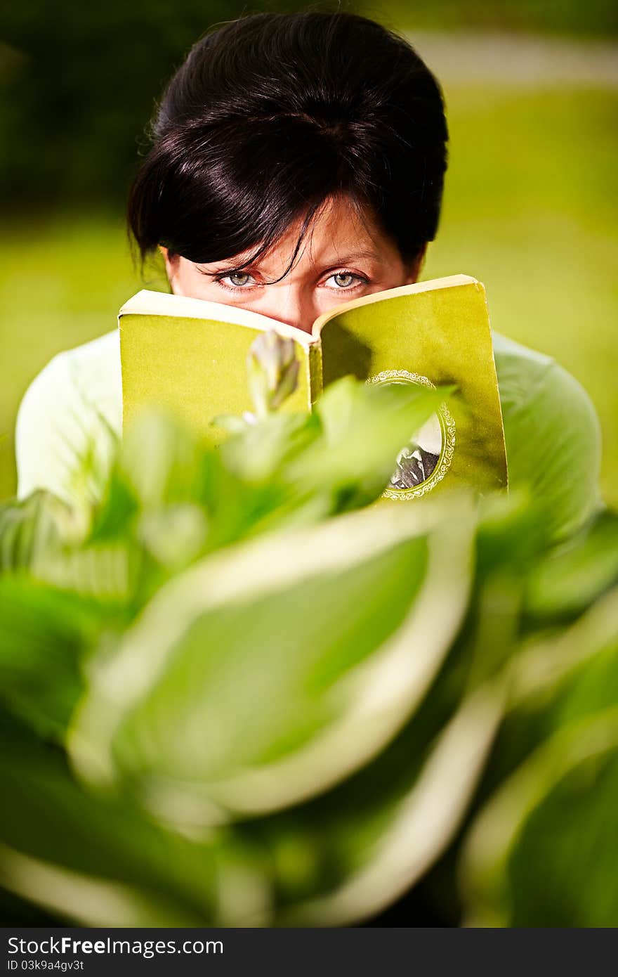 Caucasian woman is reading the green book sitting on the grass in the park. Caucasian woman is reading the green book sitting on the grass in the park