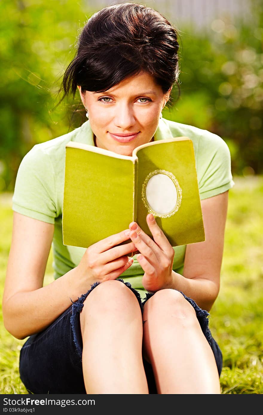 Caucasian woman is reading the green book sitting on the grass in the park. Caucasian woman is reading the green book sitting on the grass in the park