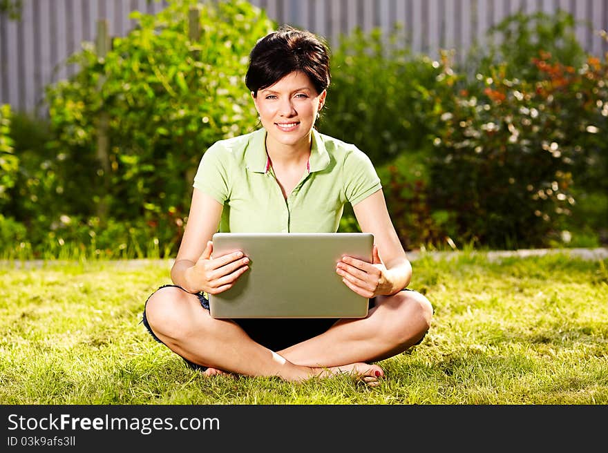 Caucasian woman is sitting on the grass with laptop. Caucasian woman is sitting on the grass with laptop