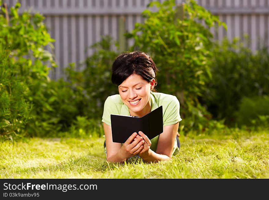 Caucasian woman is reading the green book sitting on the grass in the park. Caucasian woman is reading the green book sitting on the grass in the park