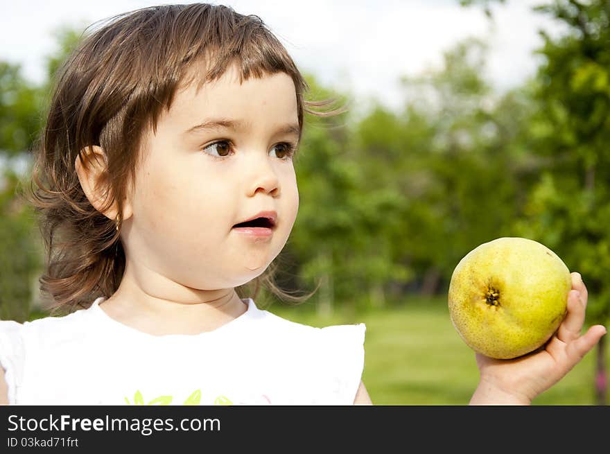 The portrait of the girl in park with pear in the hand