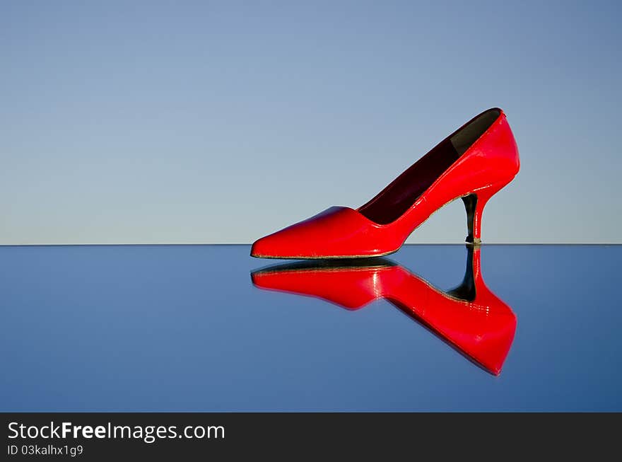 One red stiletto on mirror and sky background