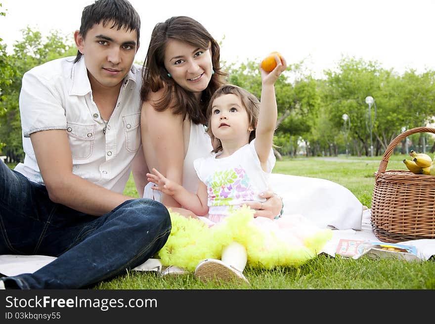 The husband, the wife and the child sit on a coverlet in park. The husband, the wife and the child sit on a coverlet in park