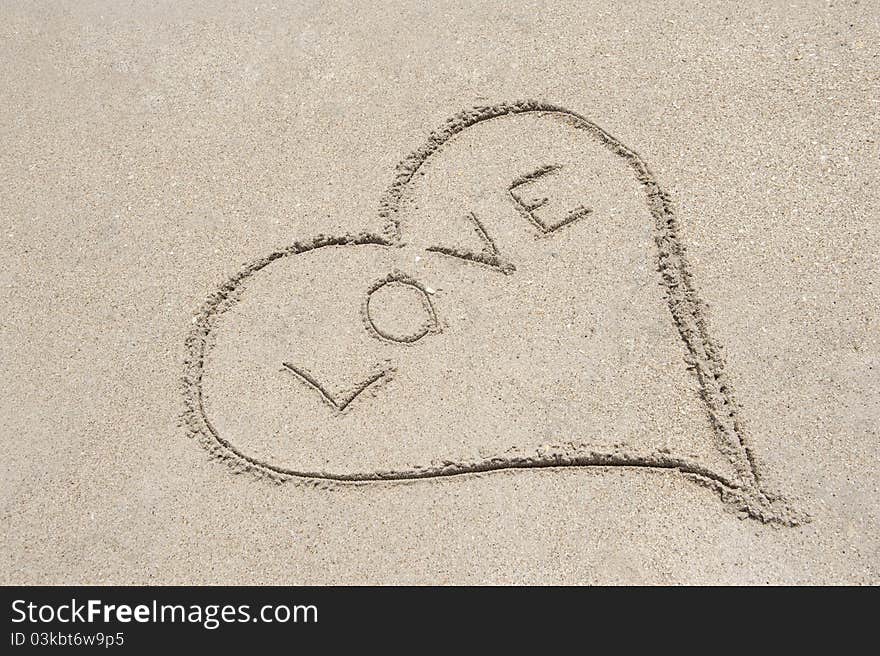 A heart shape drawn in the sand with the word LOVE written in the middle. A heart shape drawn in the sand with the word LOVE written in the middle