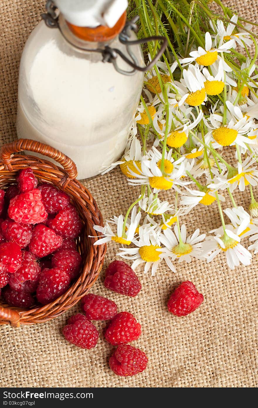 Top view on basket of fresh ripe raspberries, bottle of milk and camomile flowers on sacking. Top view on basket of fresh ripe raspberries, bottle of milk and camomile flowers on sacking