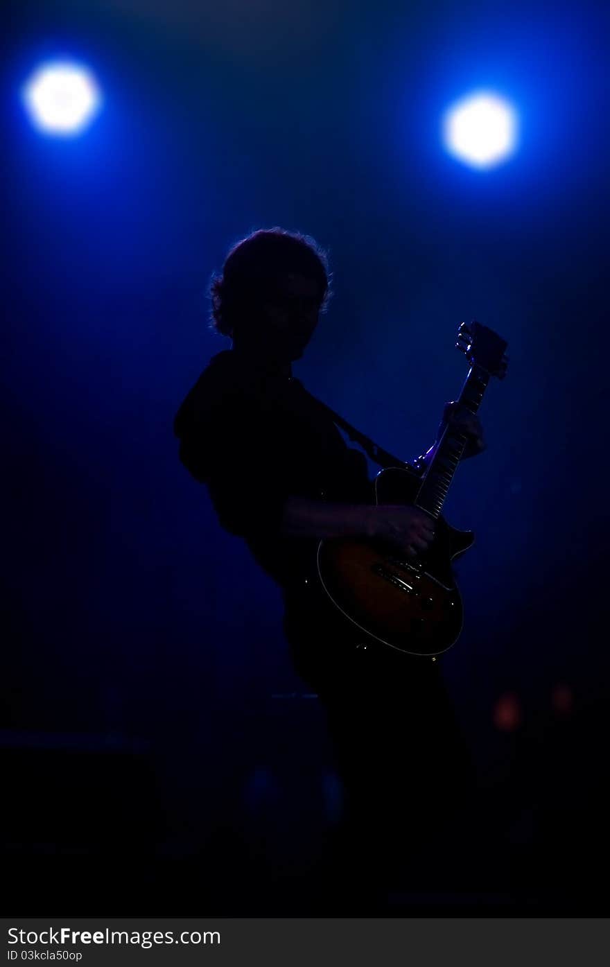 A silhouette of a musician with a guitar in bright concert light. A silhouette of a musician with a guitar in bright concert light