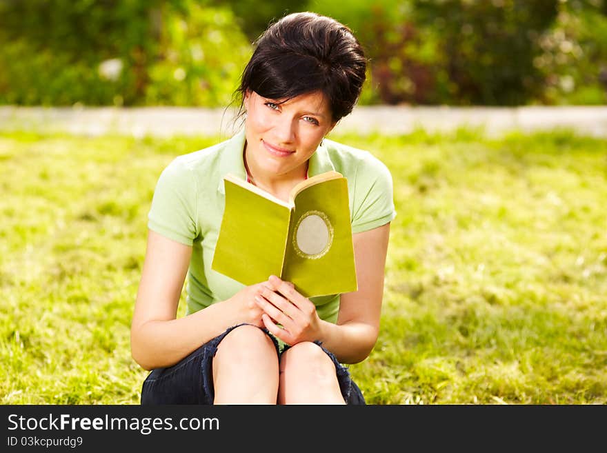 Caucasian woman is reading the green book sitting on the grass in the park. Caucasian woman is reading the green book sitting on the grass in the park