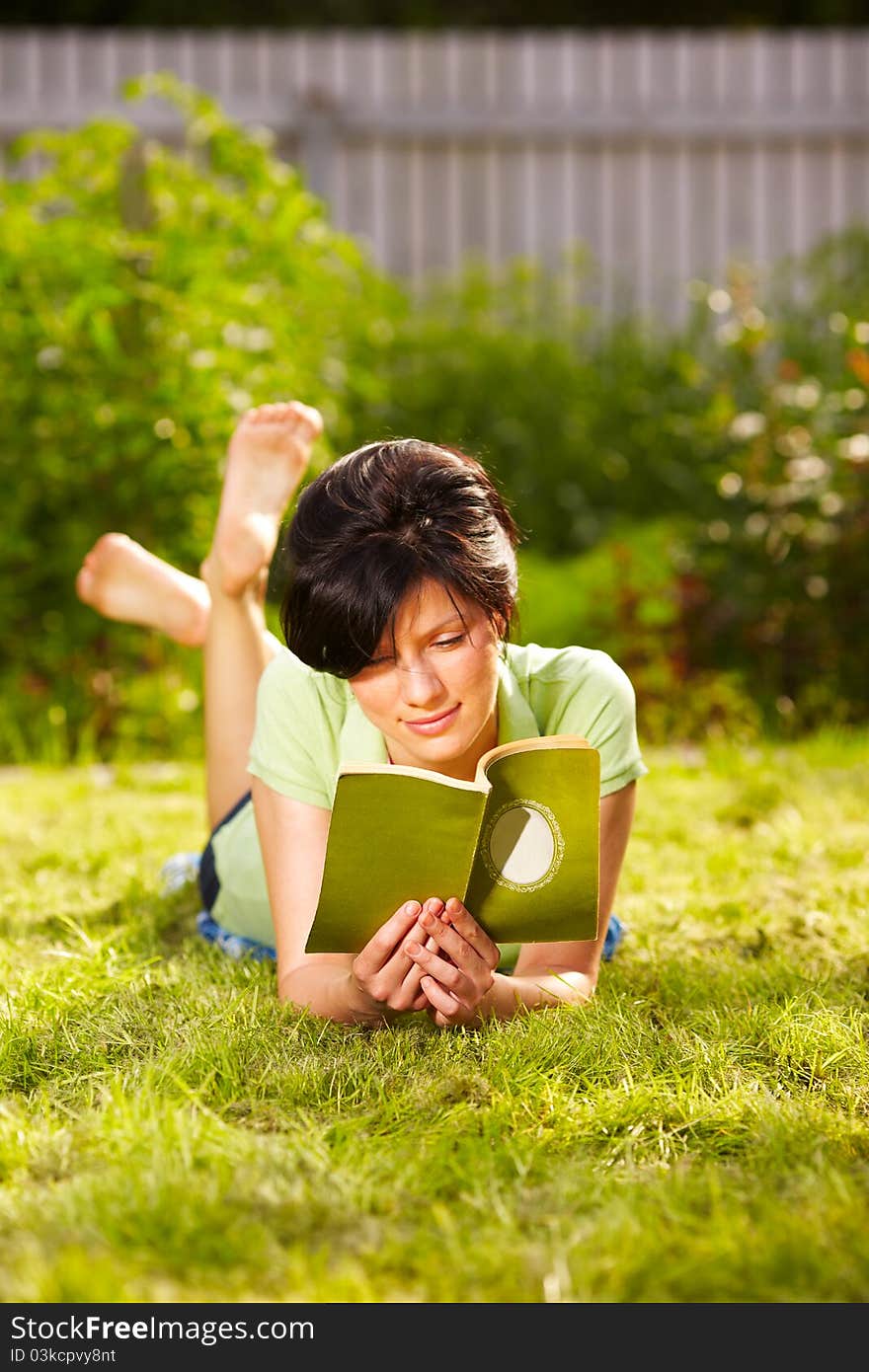 Caucasian woman is reading the green book lying on the grass in the park. Caucasian woman is reading the green book lying on the grass in the park