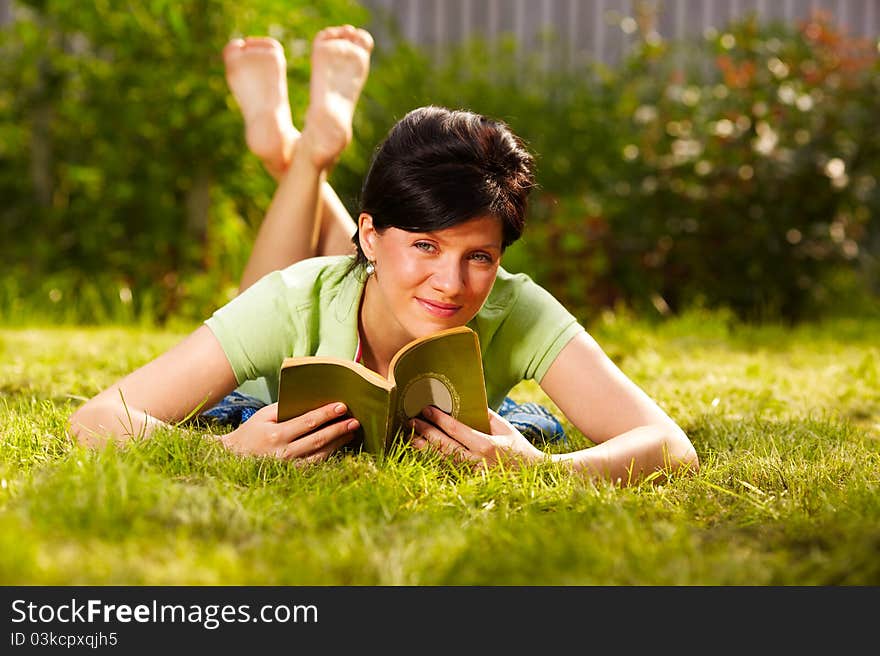 Caucasian woman is reading the green book lying on the grass in the park. Caucasian woman is reading the green book lying on the grass in the park