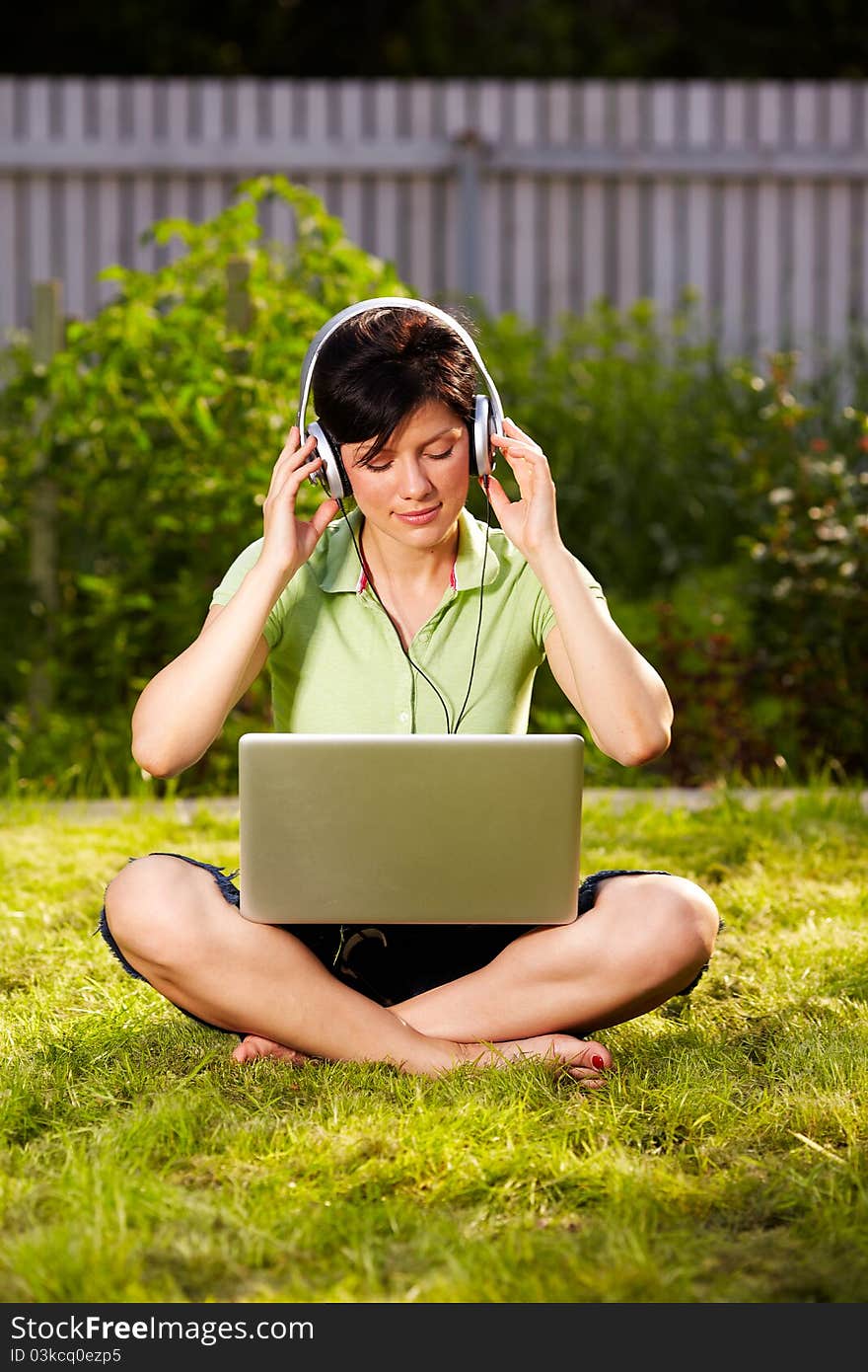 Caucasian woman is sitting on the grass wearing headphones. Caucasian woman is sitting on the grass wearing headphones