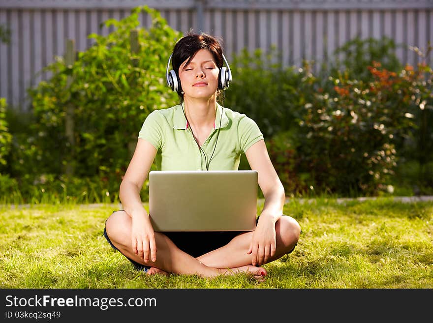 Caucasian woman is sitting on the grass wearing headphones. Caucasian woman is sitting on the grass wearing headphones