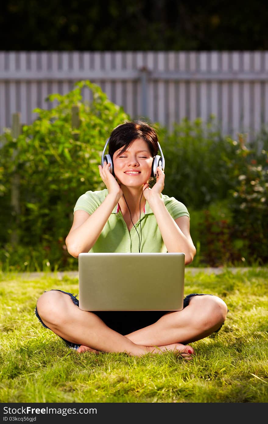 Caucasian woman is sitting on the grass wearing headphones. Caucasian woman is sitting on the grass wearing headphones