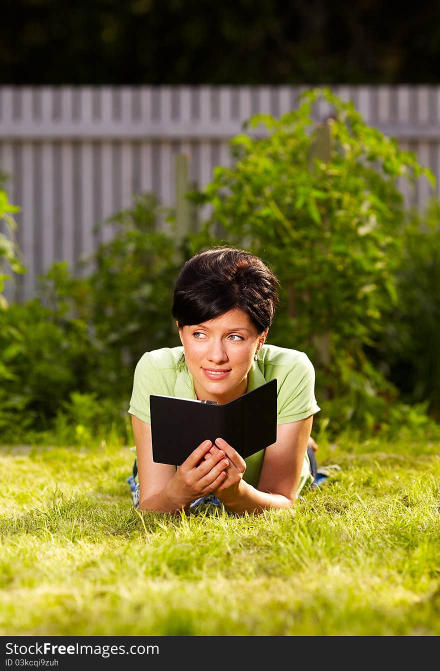 Caucasian woman is reading the e-book lying on the grass in the park. Caucasian woman is reading the e-book lying on the grass in the park