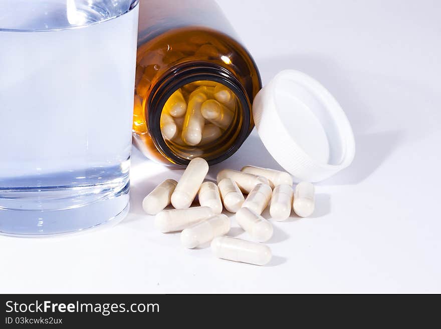 Bottle of pills with a glass of water on white background. Bottle of pills with a glass of water on white background