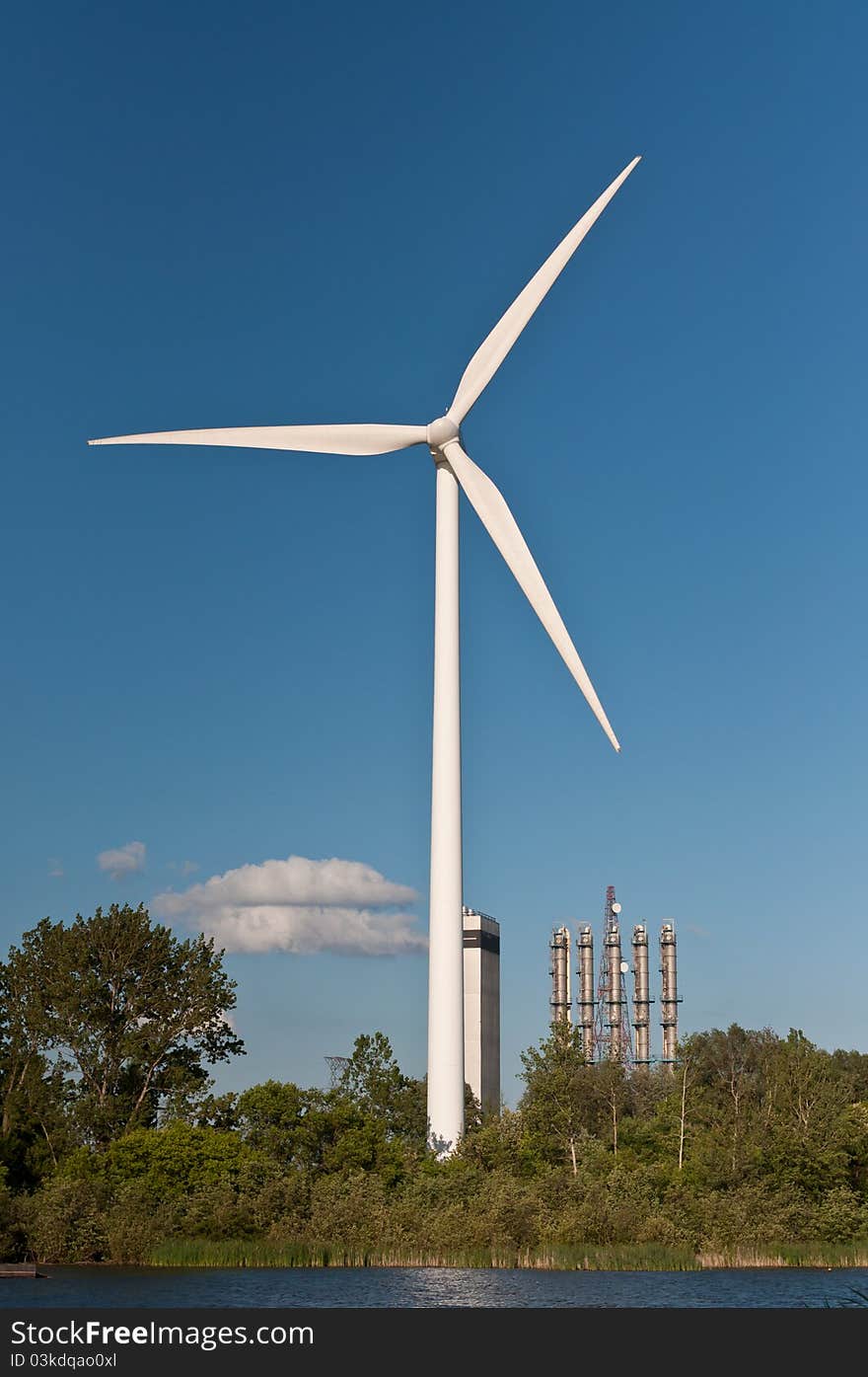 A large wind turbine stands above the treetops with a deep blue sky in the background. A large wind turbine stands above the treetops with a deep blue sky in the background.