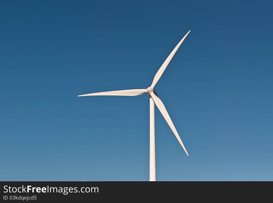 A large wind turbine spins with a deep blue sky in the background. A large wind turbine spins with a deep blue sky in the background.