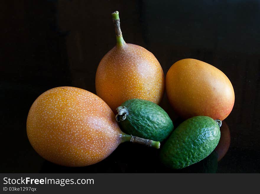 A selection of exotic fruit including granadillas, feijoas & plum mango, against a black granite background