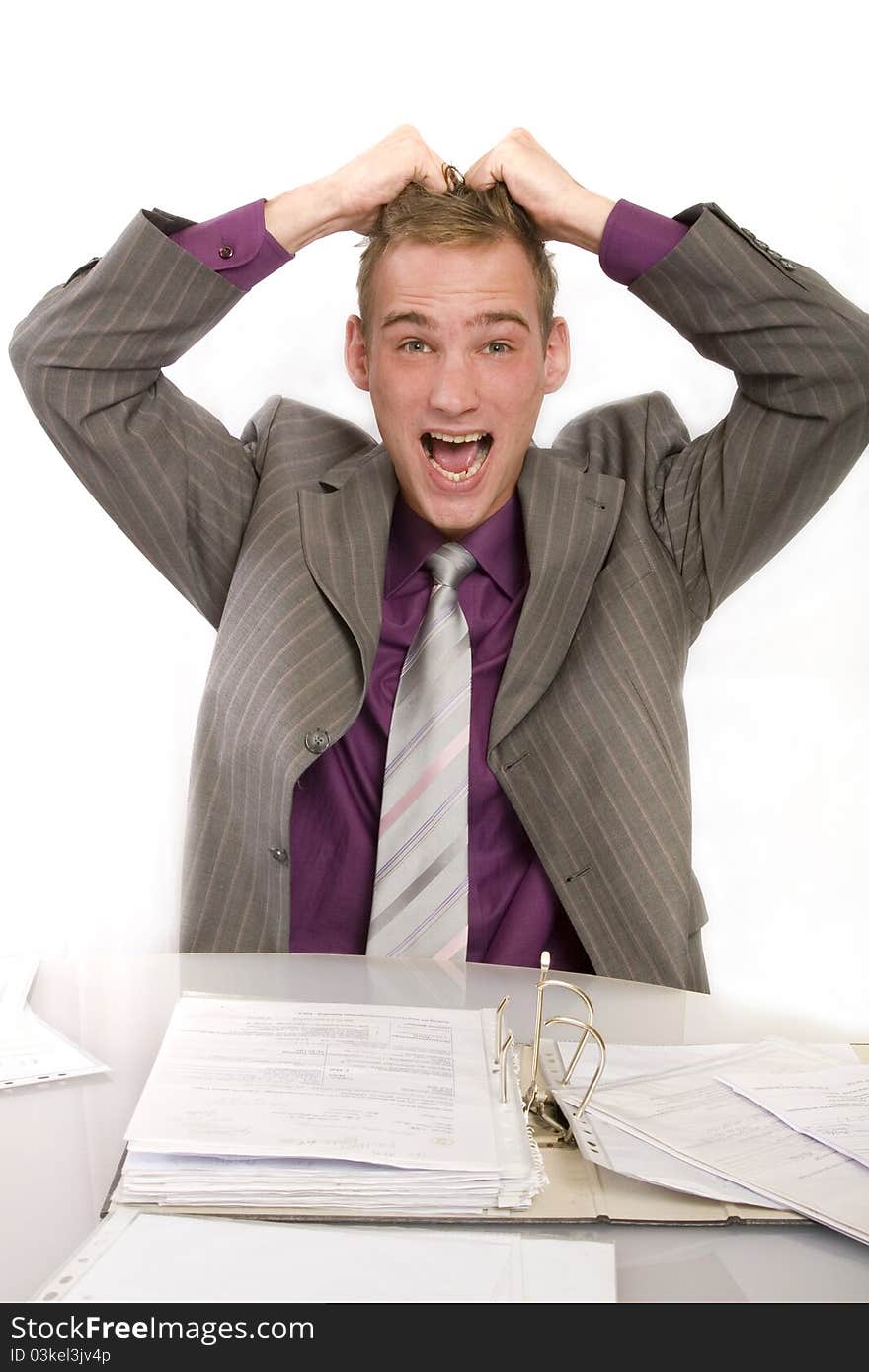 Desperate businessman at his desk in the office. He holds his hands above his head and screams. Before him a file folder.