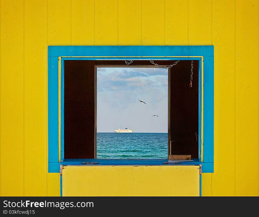 Colorful summer image of the ocean waters and blue sky framed by yellow lifeguard house window. Architectural details