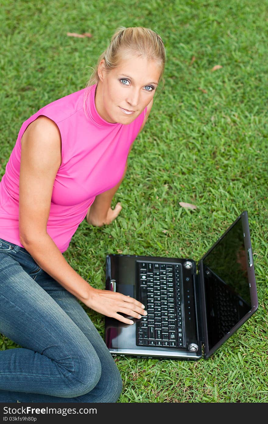 Young attractive woman works on her laptop at the park and looks up