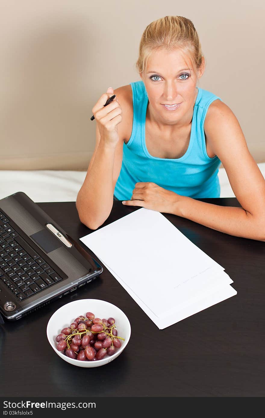 Young pretty student works on her essay with laptop beside