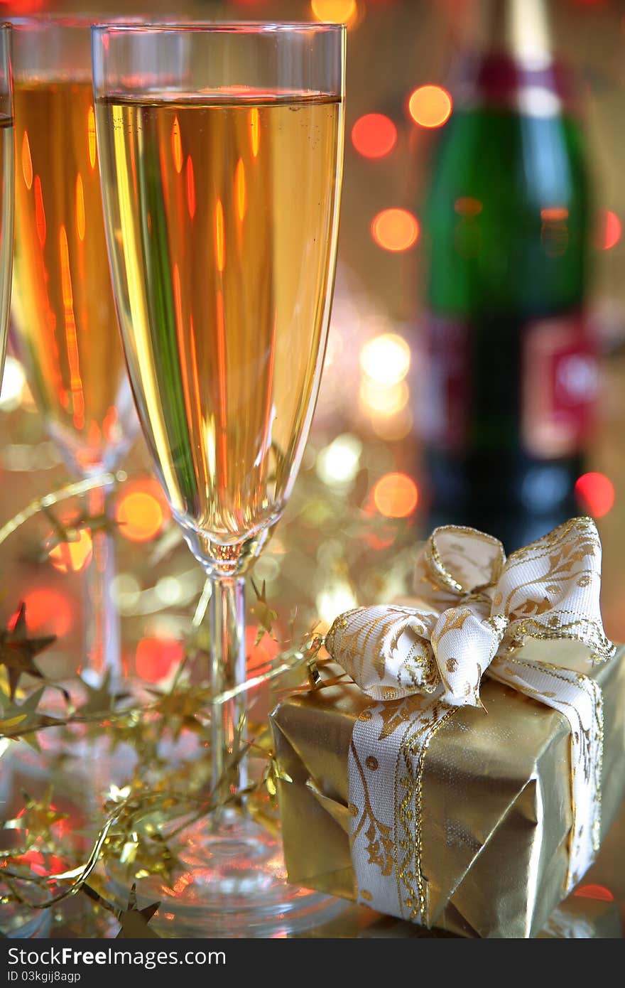 Close-up of champagne in glasses,gift box,bottle and blurredlights on background. Close-up of champagne in glasses,gift box,bottle and blurredlights on background.