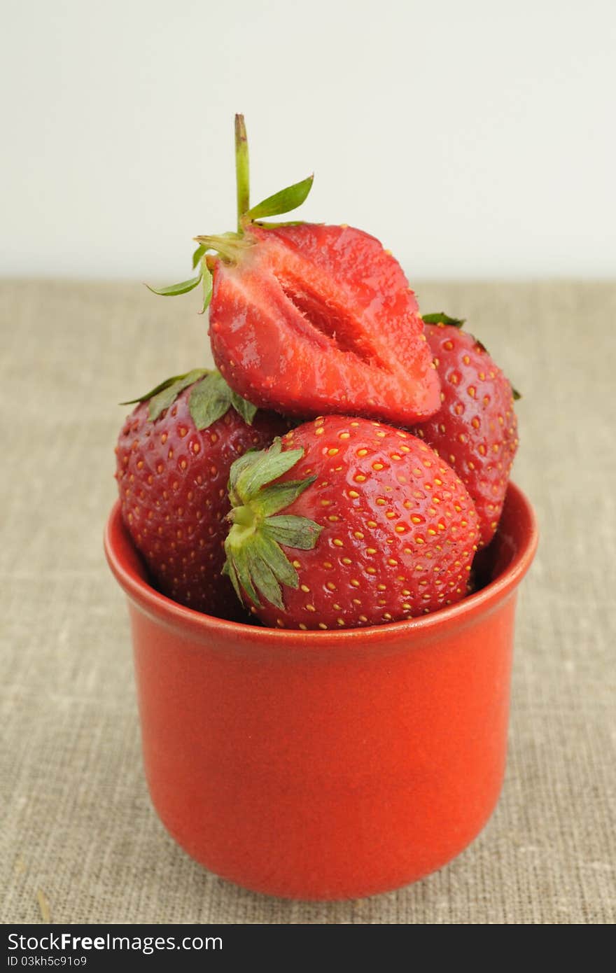 Ripe strawberries in a red cup on the background of rough cloth. Ripe strawberries in a red cup on the background of rough cloth