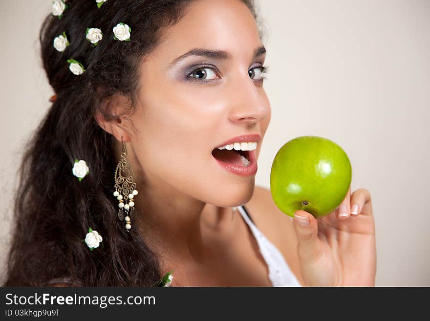 Beautiful Mixed race Woman with small white flowers in her hair eating an apple isolated on beige. Beautiful Mixed race Woman with small white flowers in her hair eating an apple isolated on beige