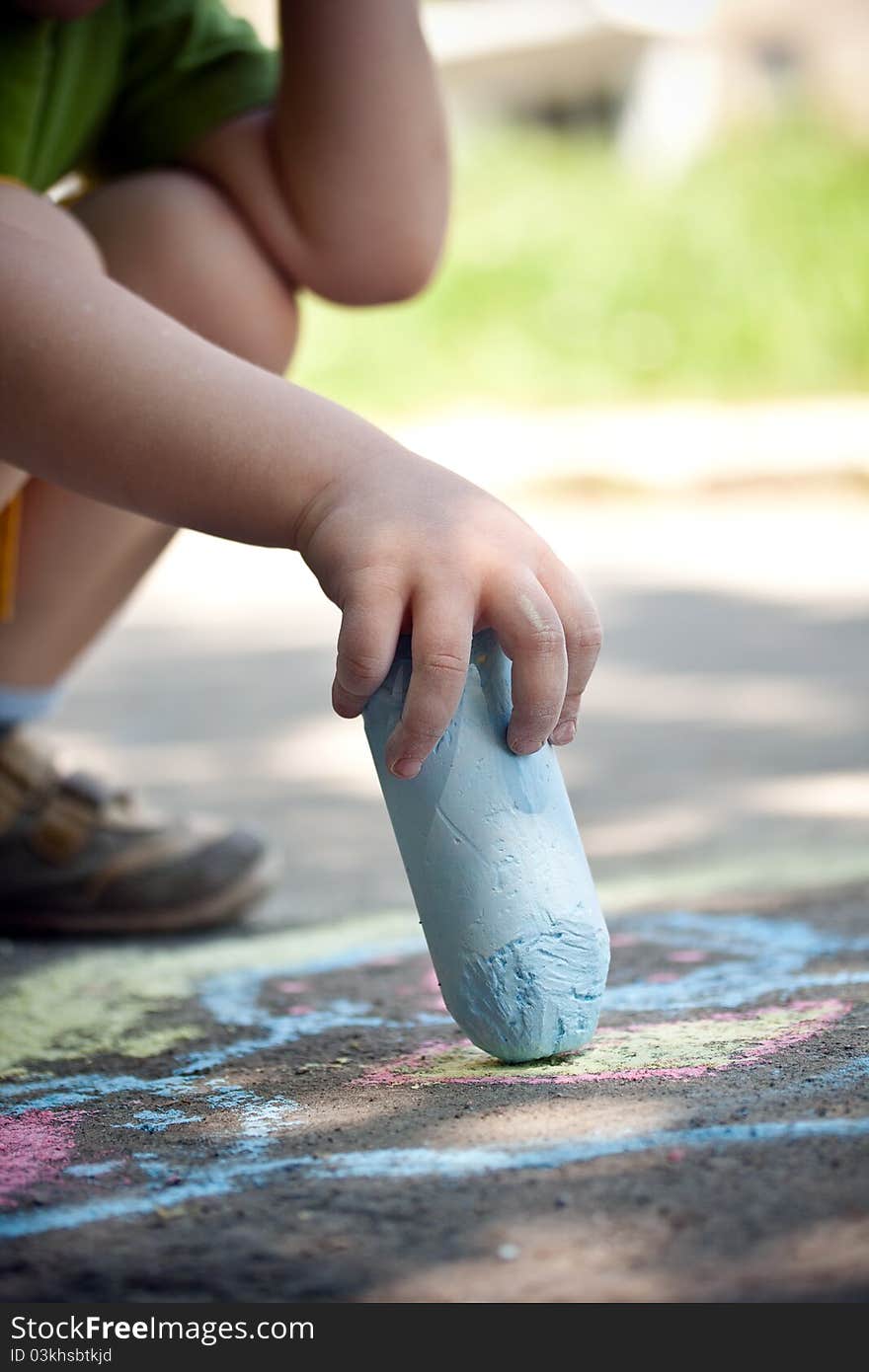 Boy drawing with chalk on asphalt focus on hand