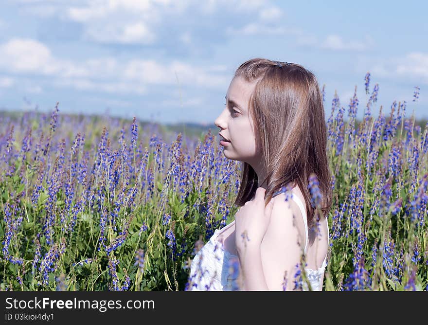 Young girl looking at the side in a meadow among flowers. Young girl looking at the side in a meadow among flowers