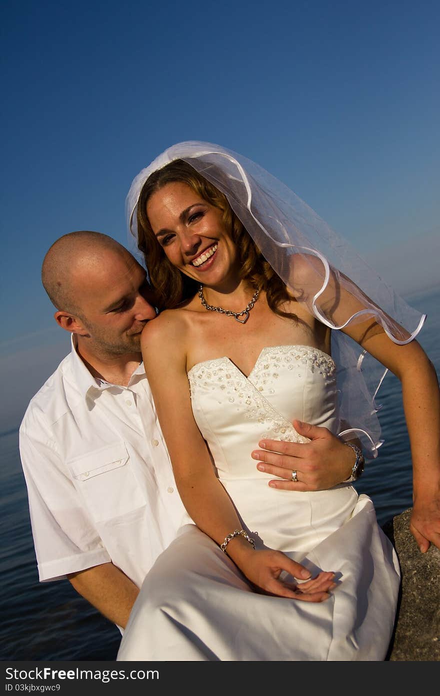 A groom kissing brides shoulder on rock at beach. A groom kissing brides shoulder on rock at beach