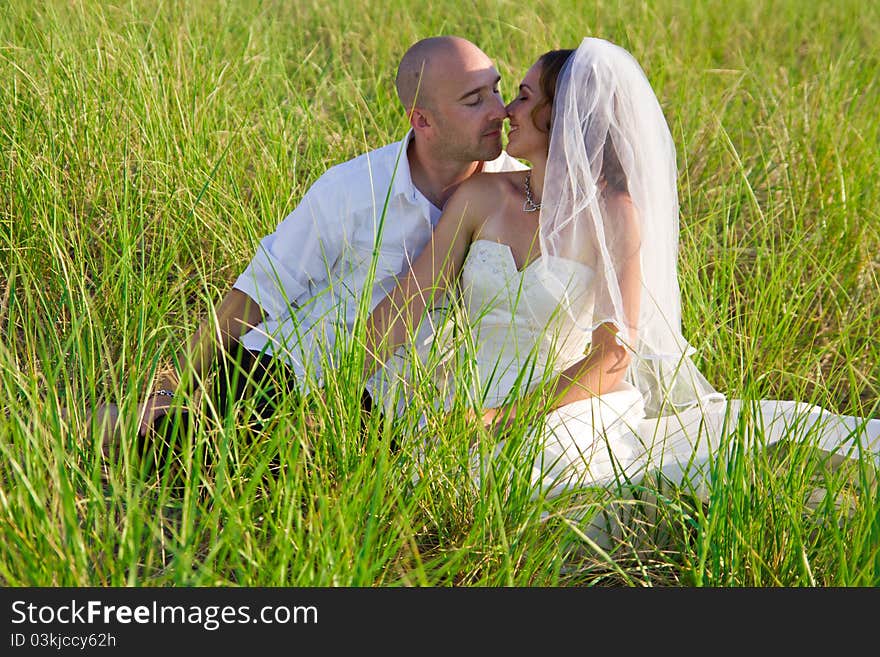 A groom kissing bride sitting in long grass