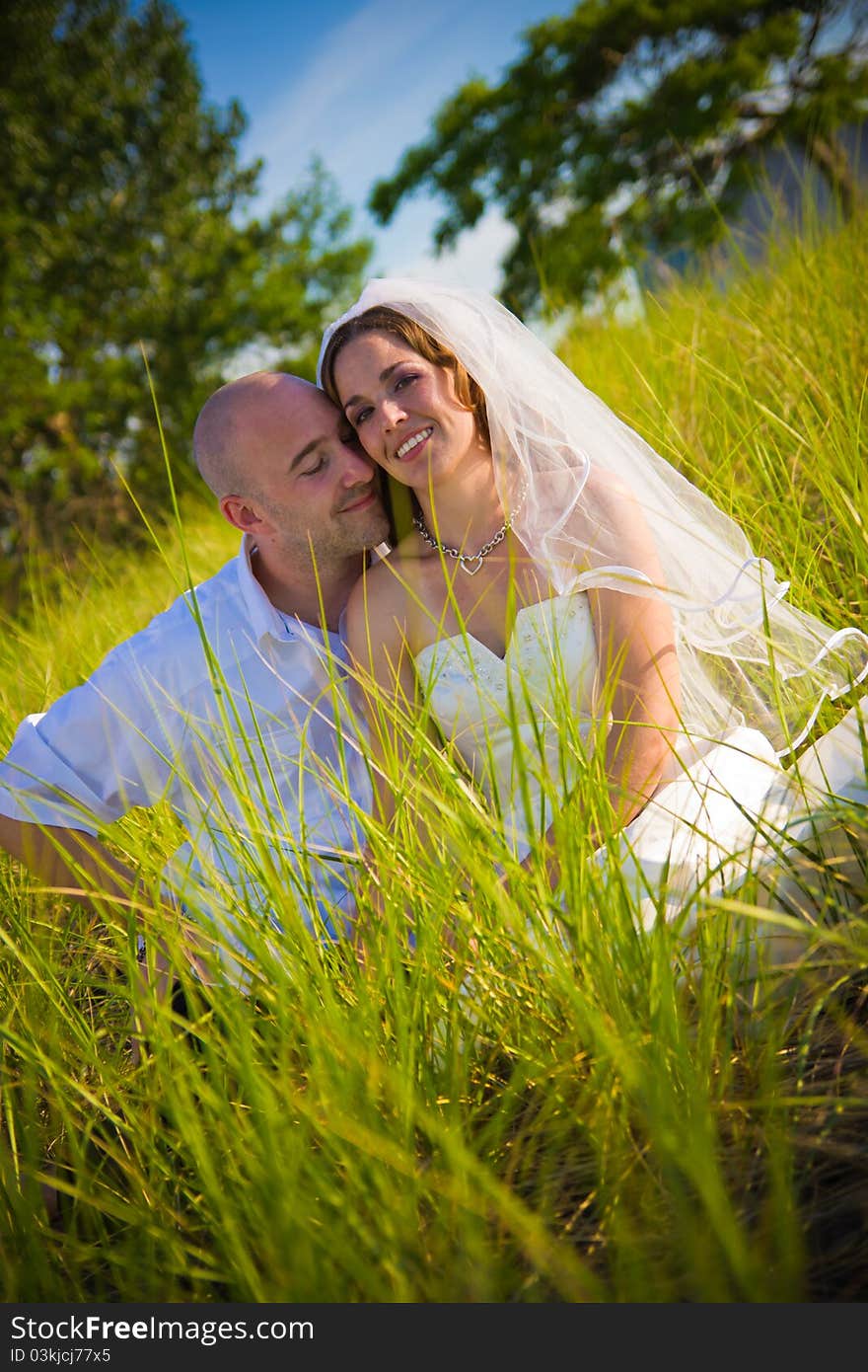 A groom and bride sitting in long grass. A groom and bride sitting in long grass