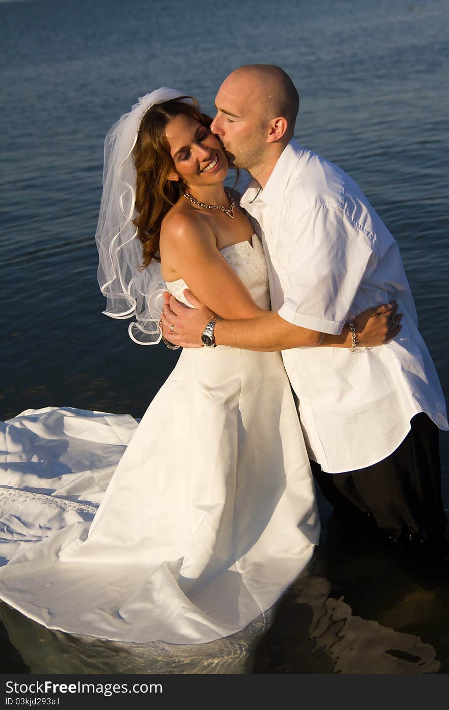 A groom kissing brides cheek while standing in water. A groom kissing brides cheek while standing in water