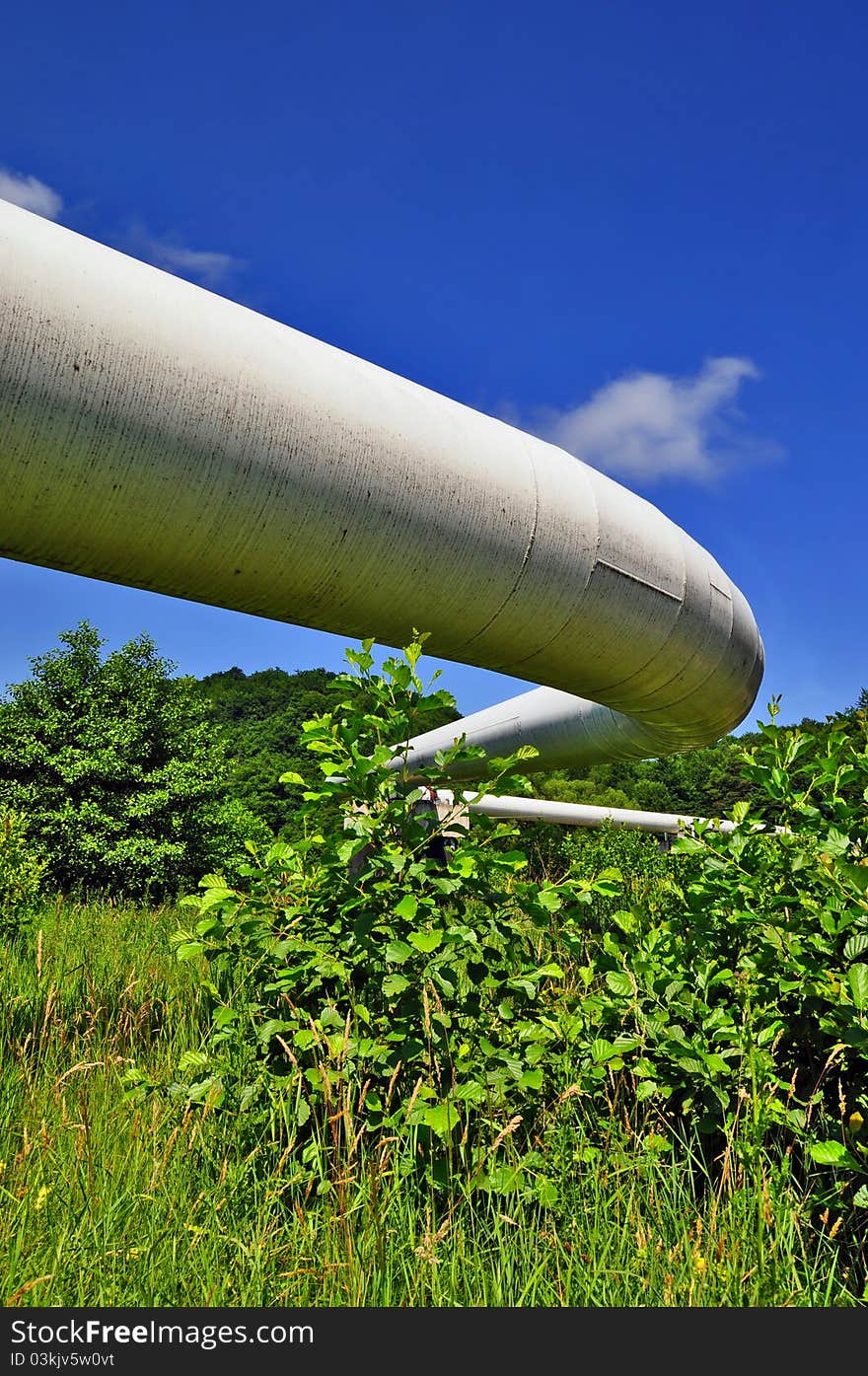The high pressure pipeline in a summer landscape with the dark blue sky and clouds
