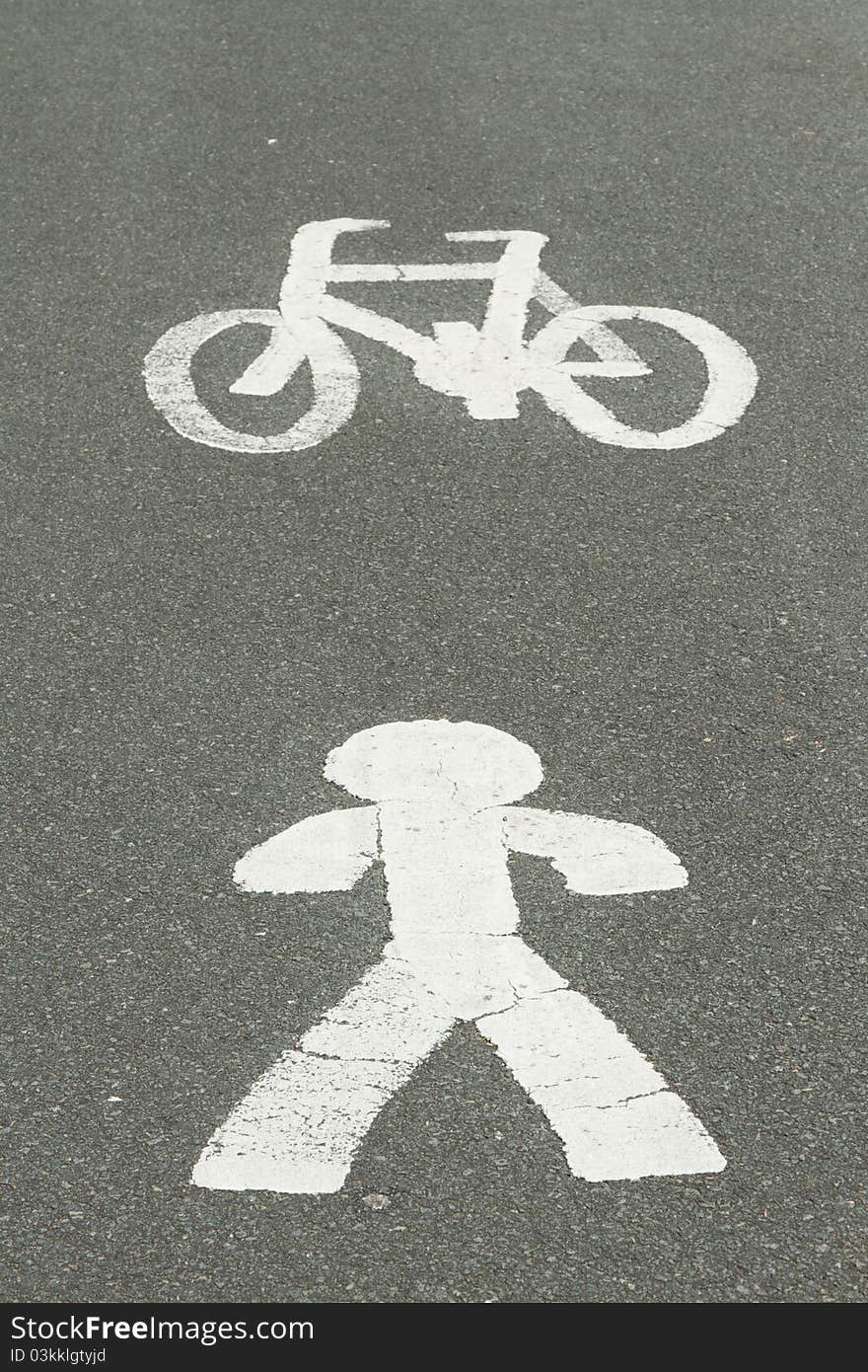 White painted symbols depicting a person and a bicycle on a grey surface of a tarmac track. White painted symbols depicting a person and a bicycle on a grey surface of a tarmac track.