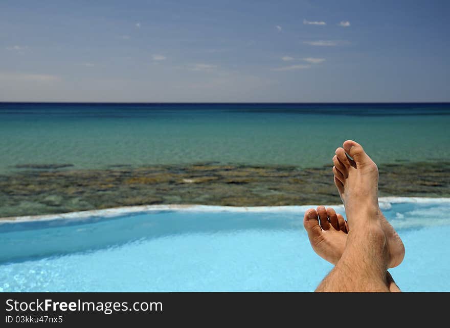 Picture of male legs over swimming pool and sea in the background