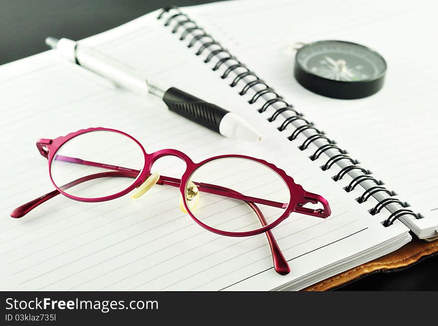 Notebook with pen and glasses on a black background