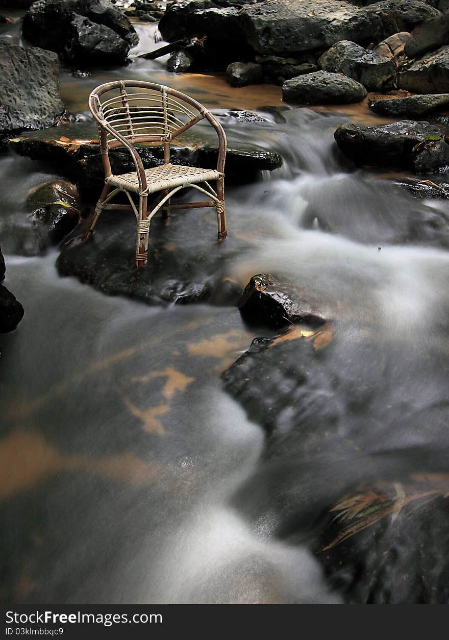 Long exposure rattan chair at waterfall create slow motion water flow. Chair face to right side. position chair at top left at image.